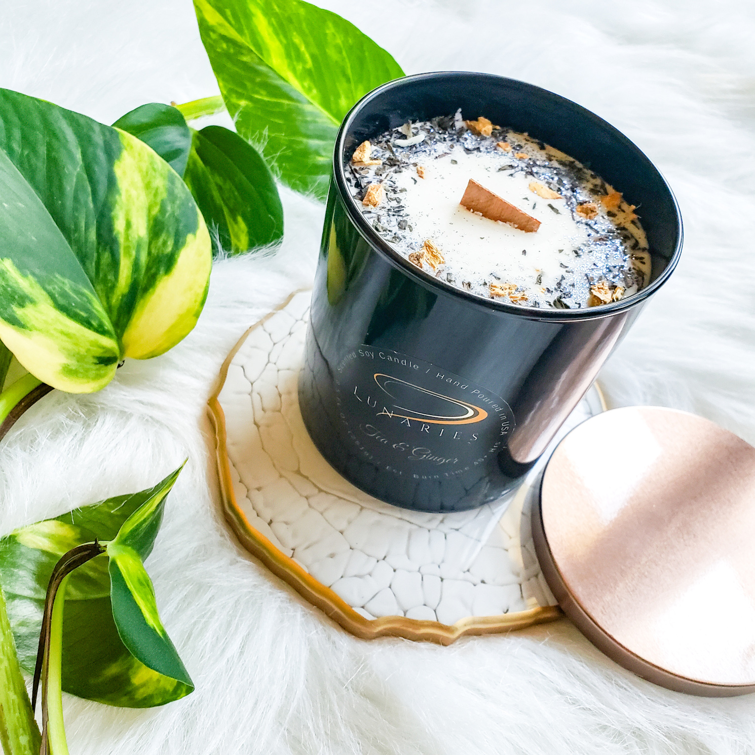 White Tea soy candle in a black glossy tumbler jar, featuring a wooden wick and decorated with white and cream dried flowers, botanical grasses, and a touch of green tea for contrast.