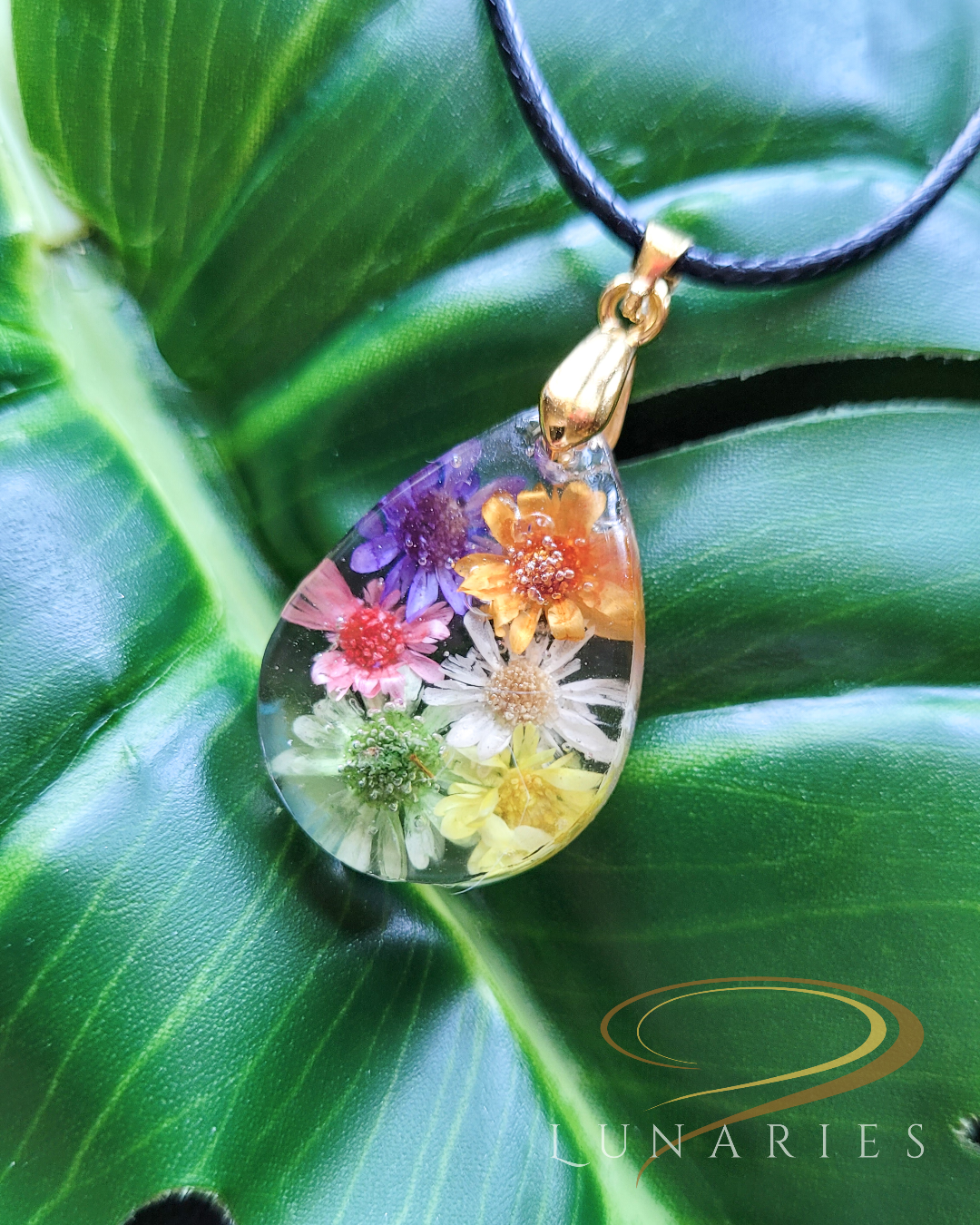 Clear resin pendants in a teardrop shape with six colorful real dried flowers golden pinch bail and black waxed cord with golden clasp
