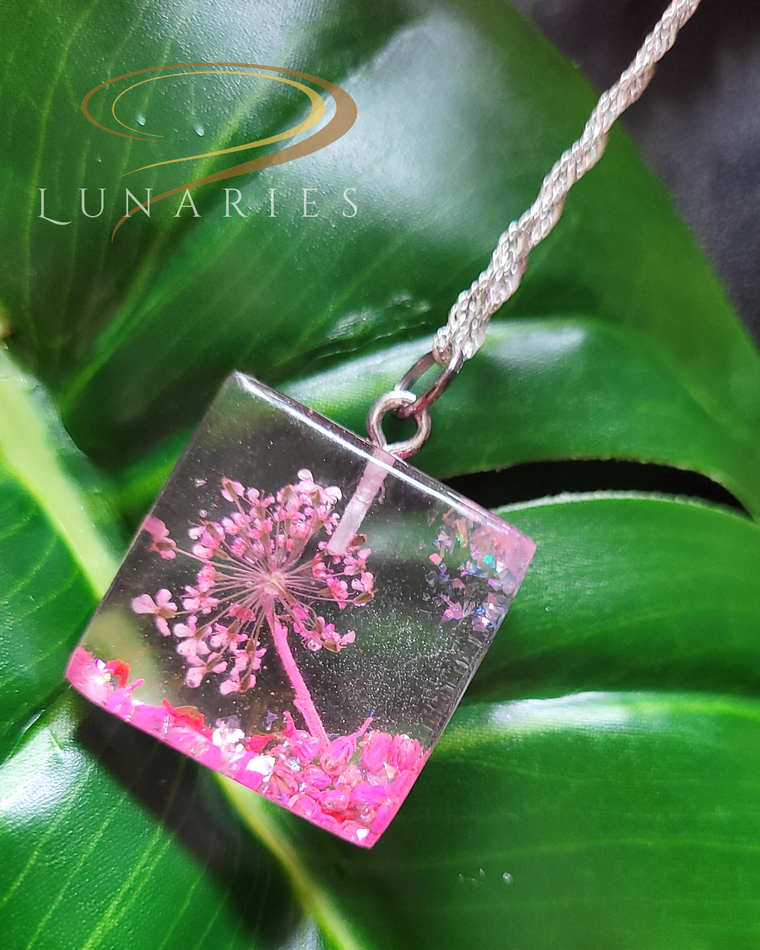 square resin pendant with real pink flowers and pink glitter showing little landscape of a tree on a hill