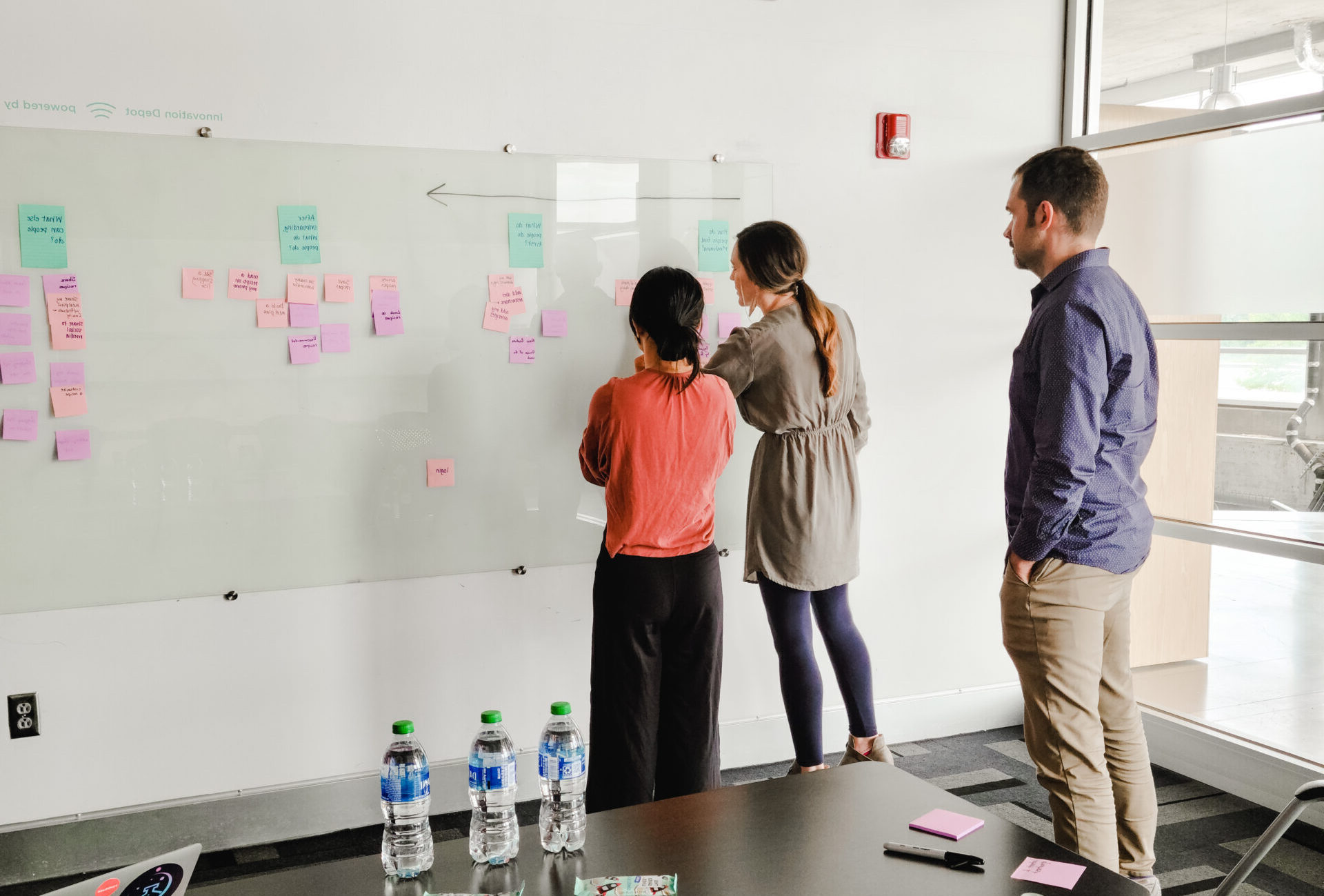 2 Founders and a facilitator post sticky notes to a whiteboard