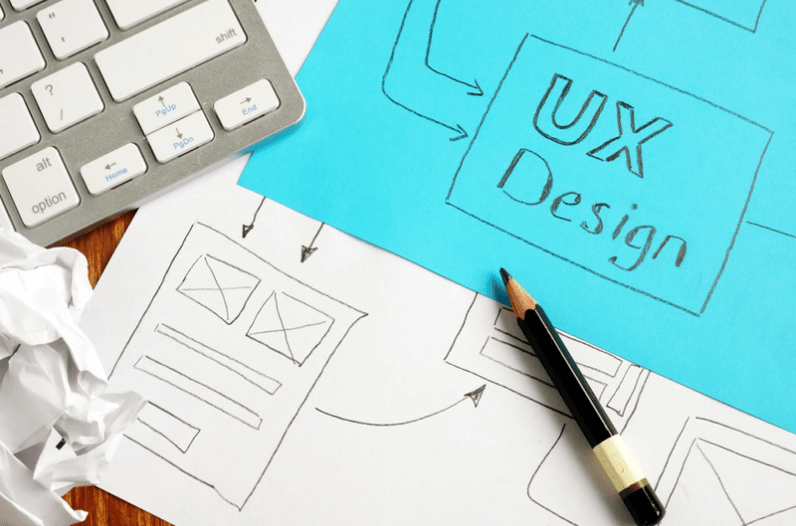 desk top with a laptop keyboard, a pencil, and drawings of wireframes including one labeled "UX Design"