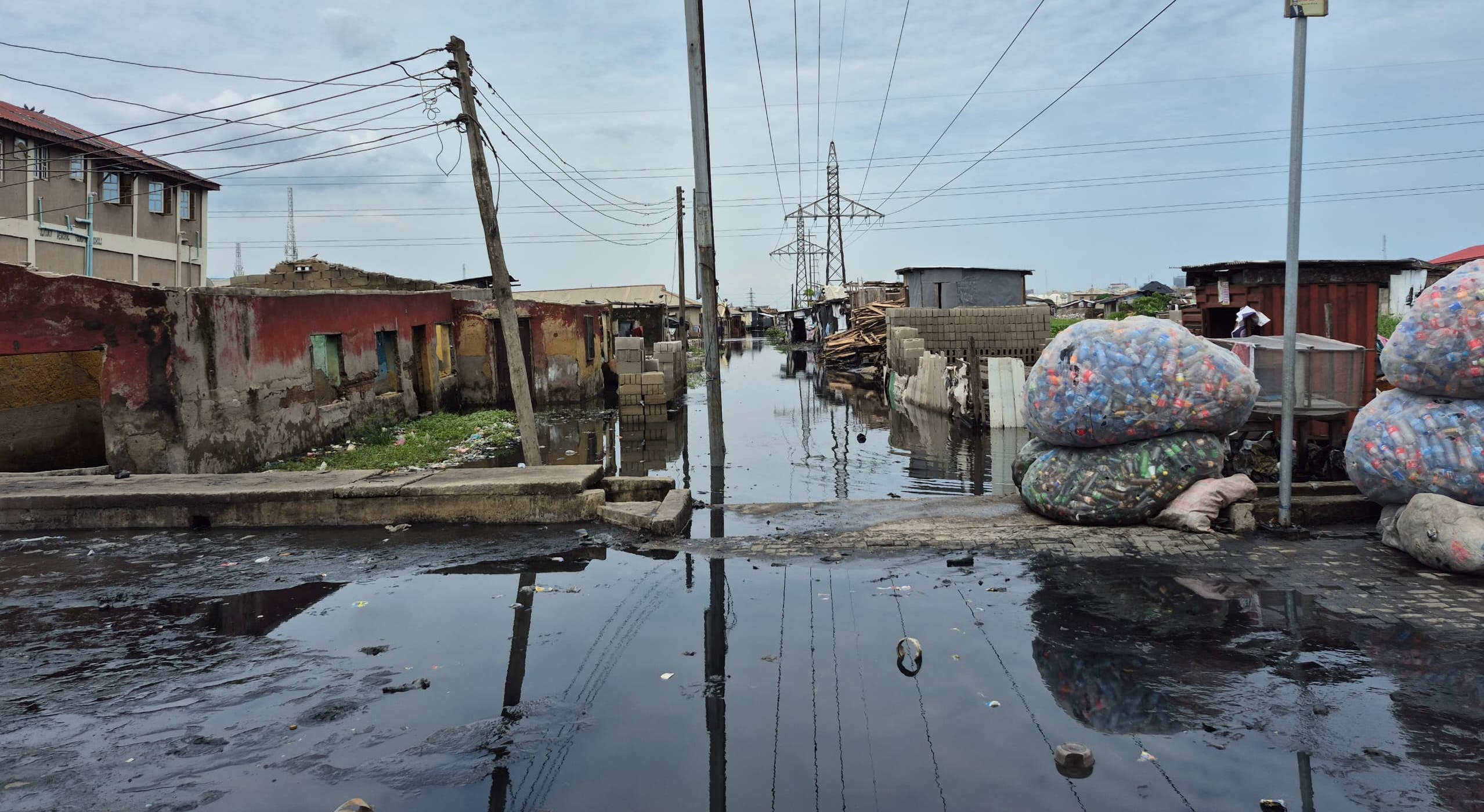 A flooded street lined with homes and power lines highlights the poor living conditions of many residents in Ajegunle, Lagos (Photo credit: Mariam Ileyemi)