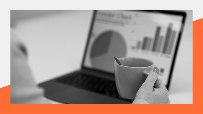 Person holding a coffee mug in front of a laptop displaying charts and graphics.