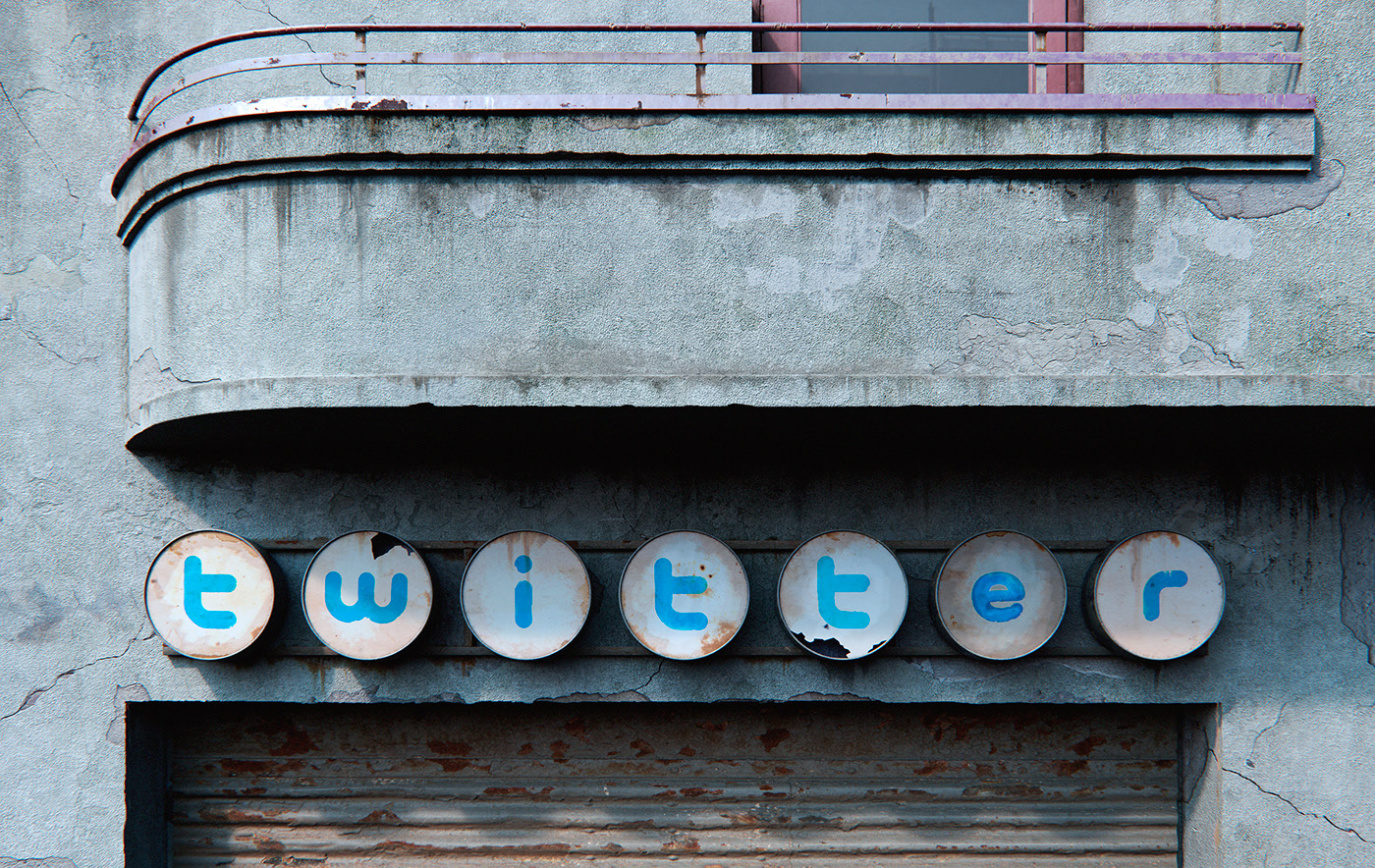 A mid-century imagining of a Twitter company sign on the side of a commercial building, but aged to the point that the sign is rusted, broken, and decaying from neglect