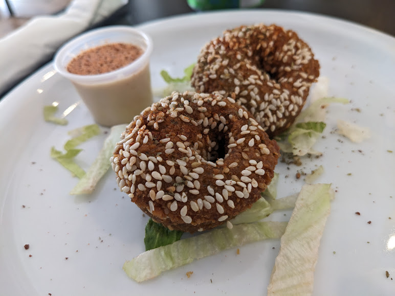 Two bagels on a plate with lettuce and dipping sauce.