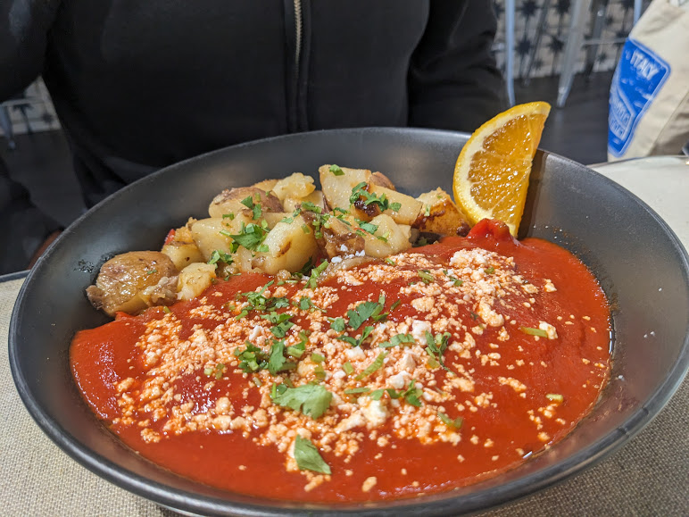 A bowl of tomato soup with potatoes and an orange slice.