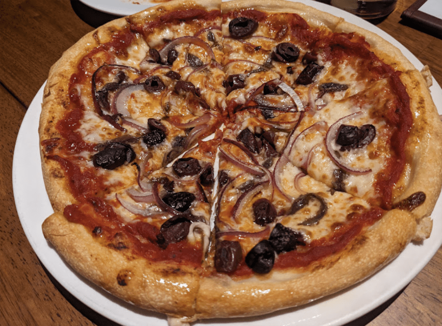 A pizza with olives and onions on a plate at Luisa's