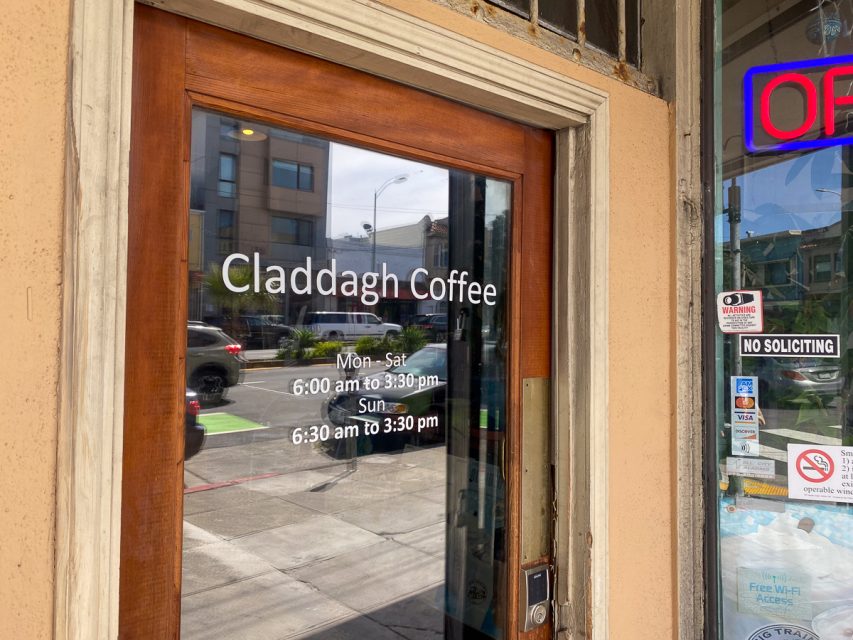 克拉达咖啡店的玻璃门入口处有街道的倒影，显示营业时间并提供免费无线网络。