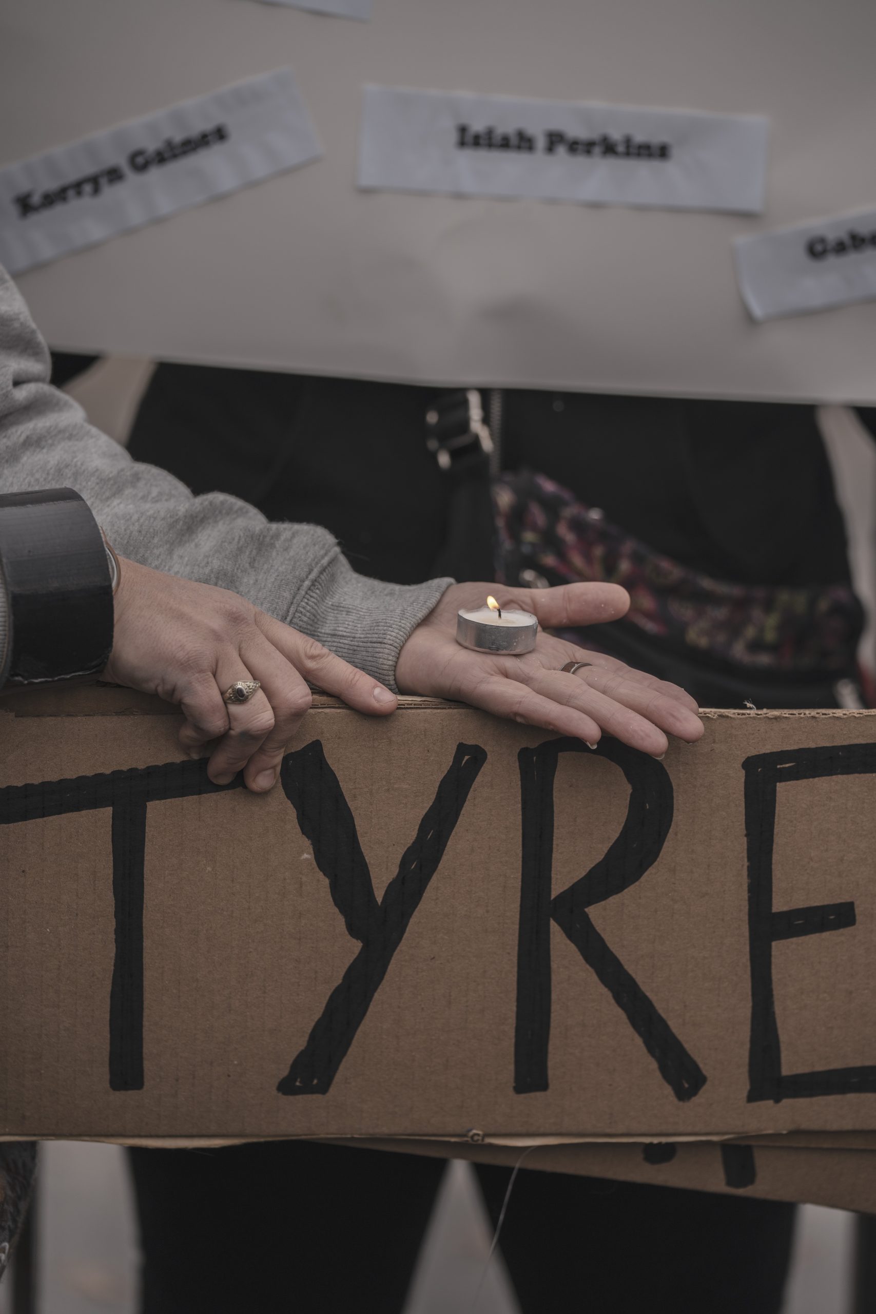 A person holds a lit tea light candle in their palm above a sign reading Tyre.