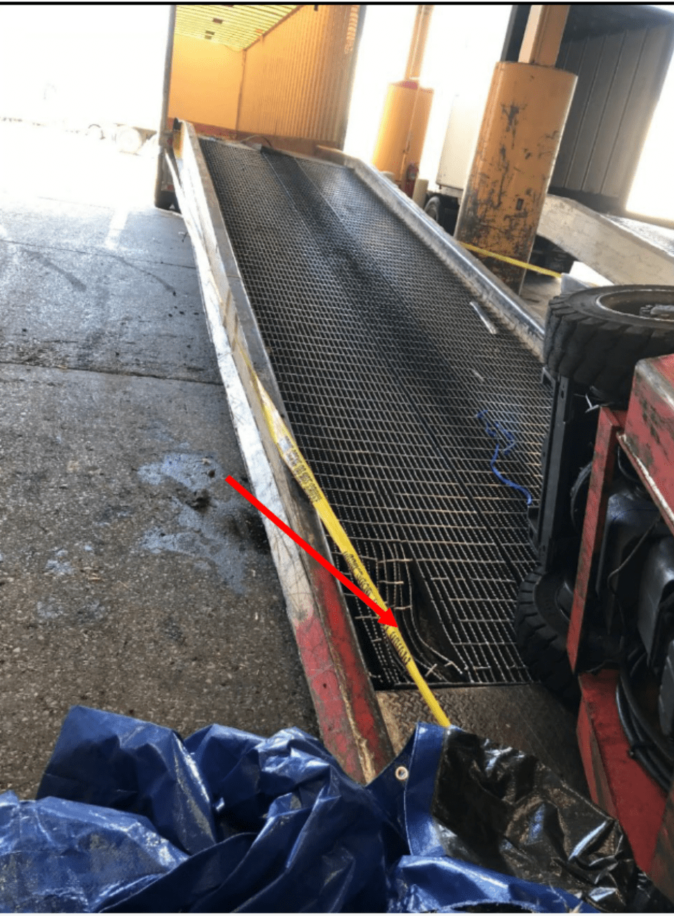 A metal ramp with an overturned forklift at its base. A red arrow points to a damaged portion of the ramp. 