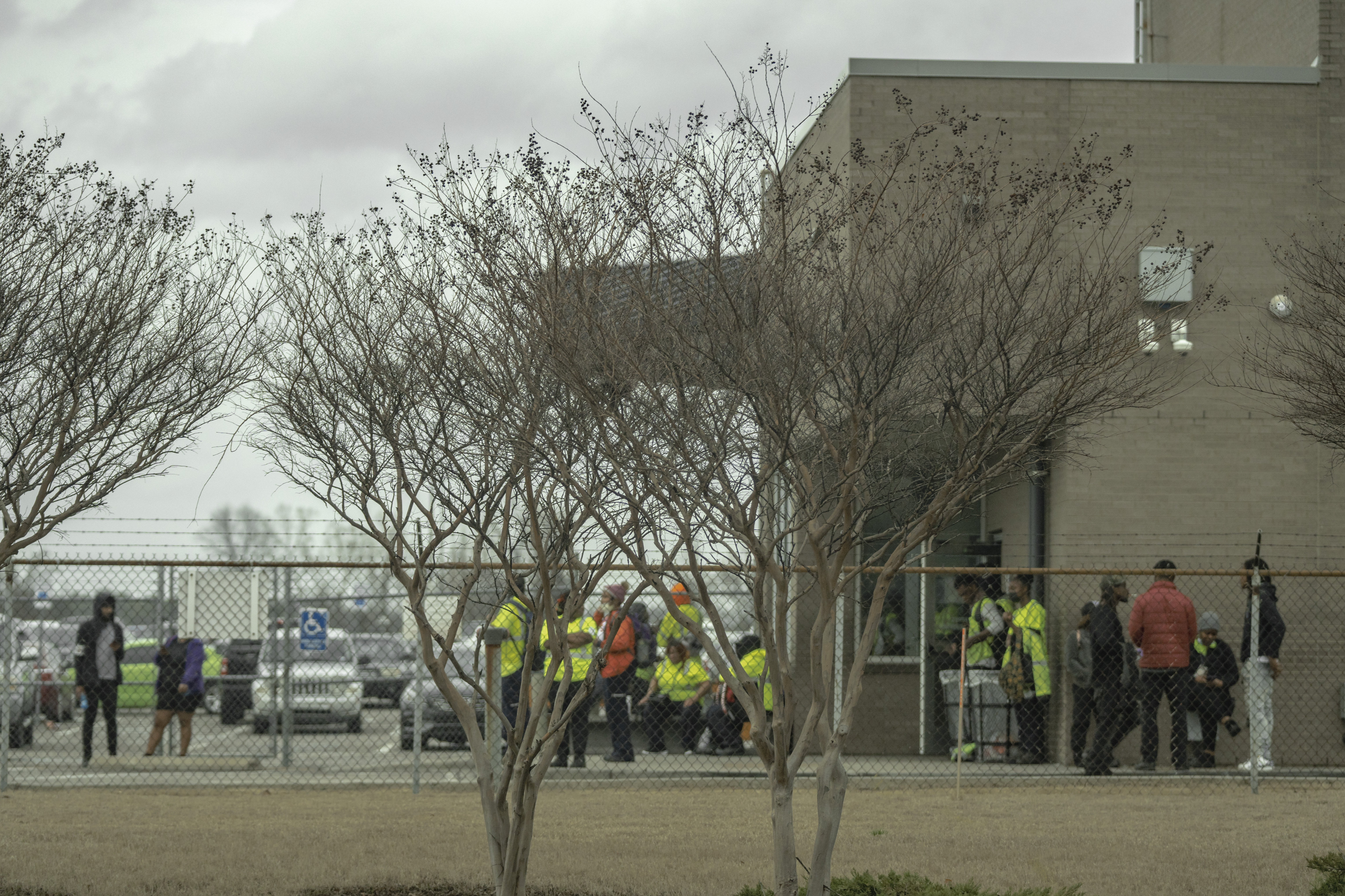 Workers in bright yellow shirts stand outside a brick building.