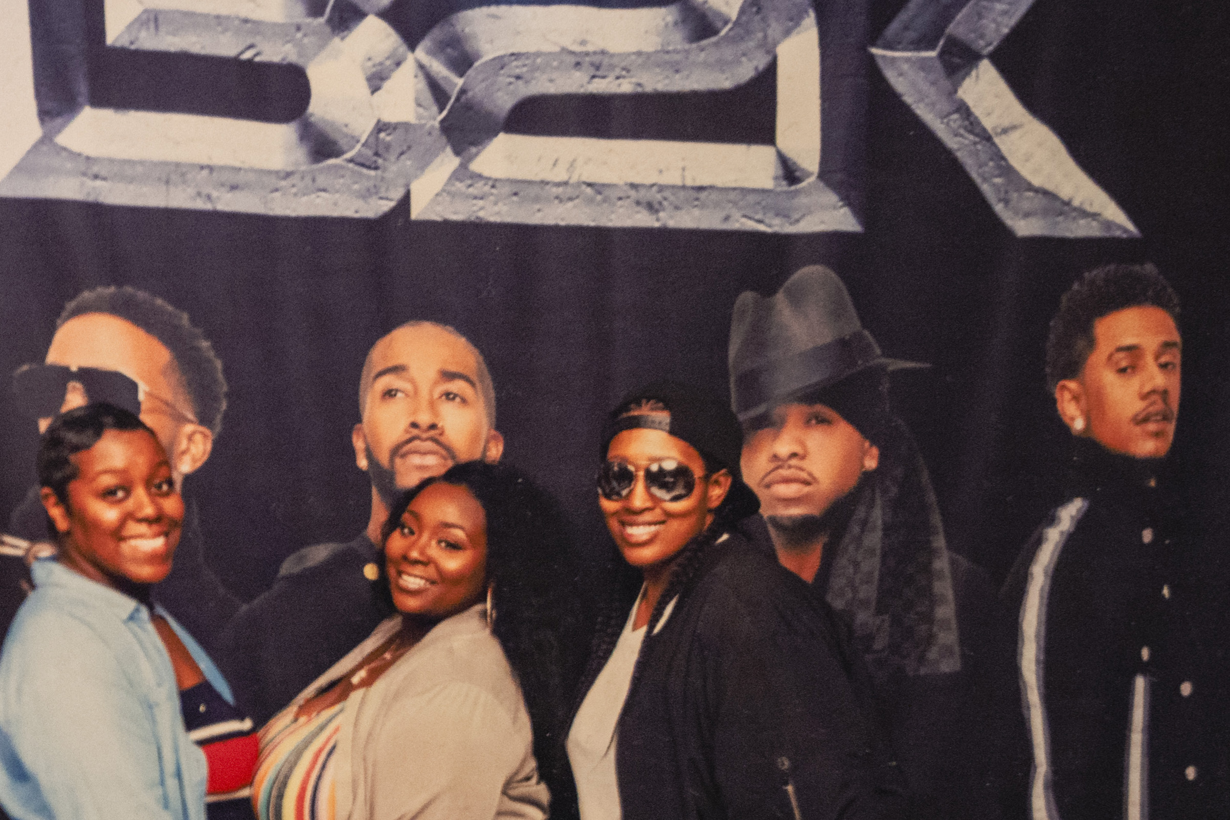 Three Black friends stand in front of a B2K backdrop. 