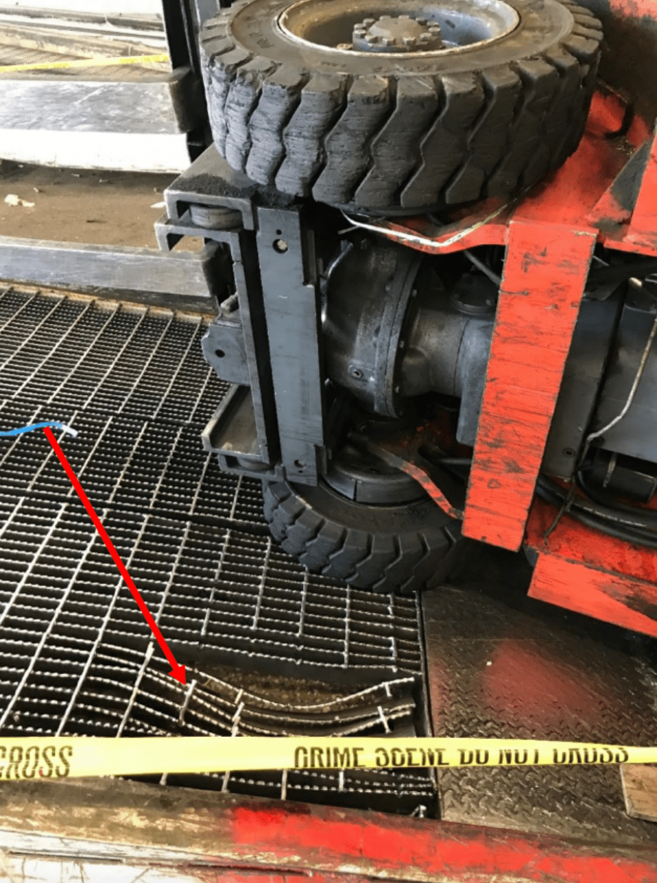 An overturned forklift on a damaged metal ramp. An arrow points to a damaged portion of the ramp. 