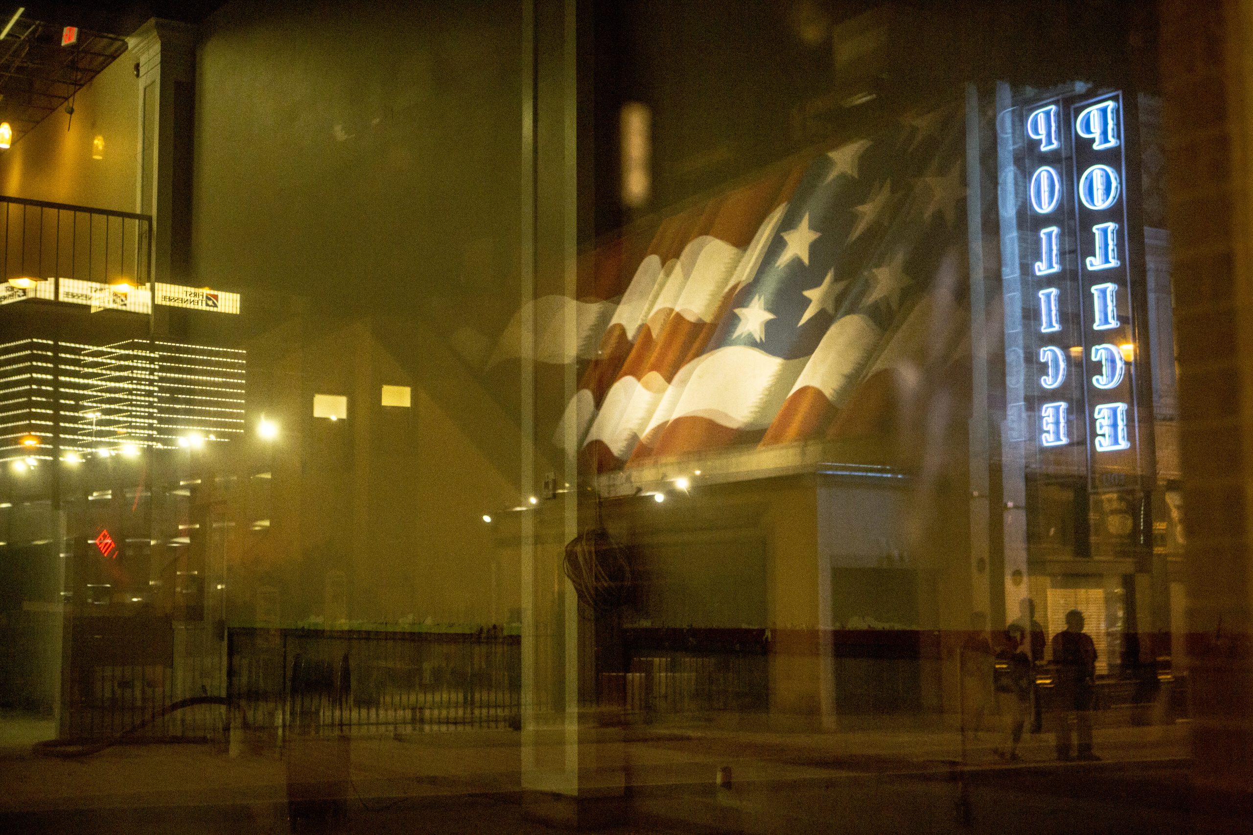 A neon sign reading "Police" is reflected on an empty storefront window on Beale Street.