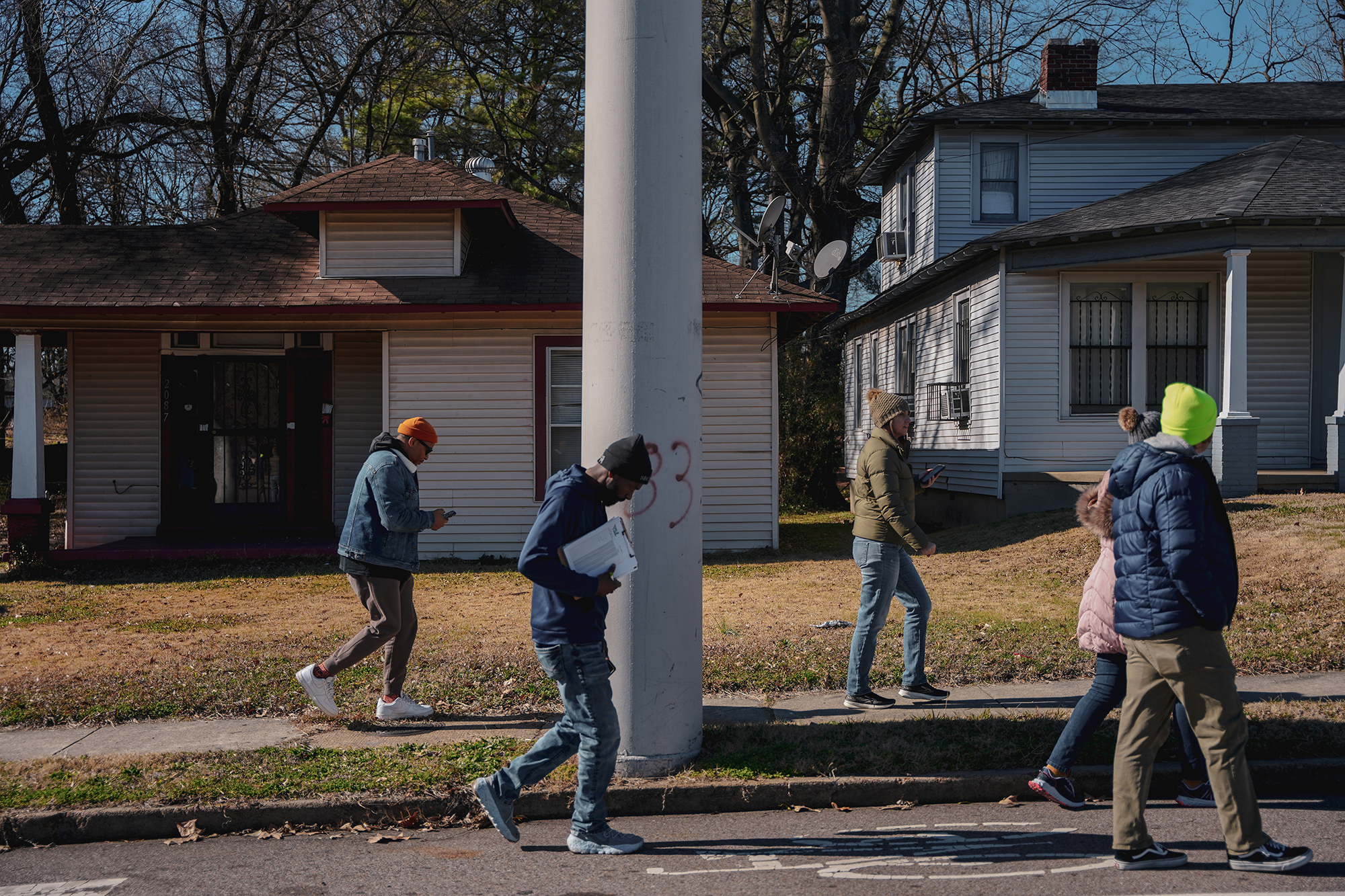 A group of people walk along the sidewalk and road in a residential Memphis neighborhood. 