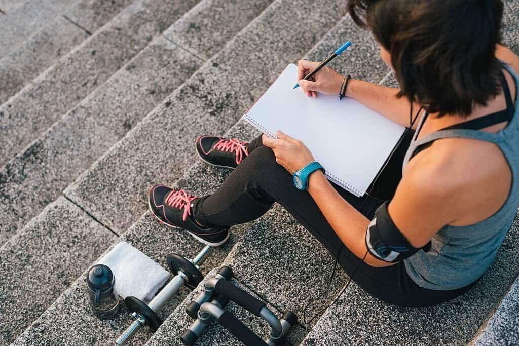Athlete in the city who is focused on her goals scribbling on a notebook
