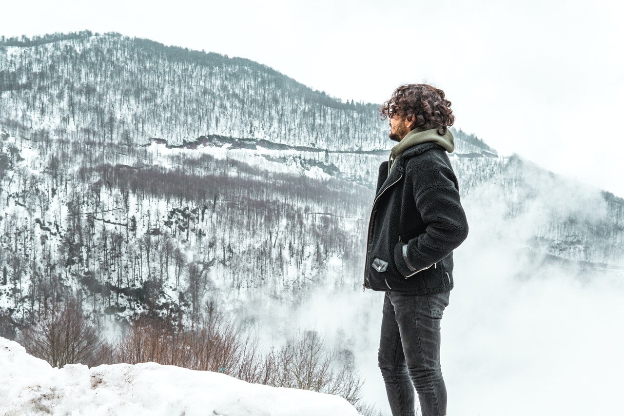 Tenacious man in black jacket looking at the snow mountains