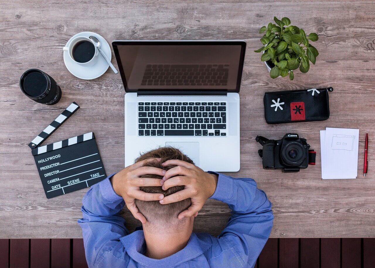 Man sitting on office tablet with laptop, holding his head due to headache