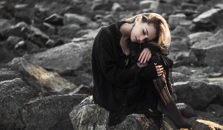 Lonely and sad woman setting on rocks in a beach