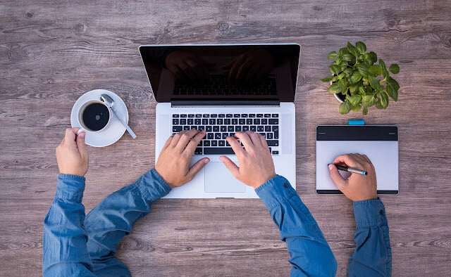 Man with blue full sleeve shirt with four hands working on his macbook