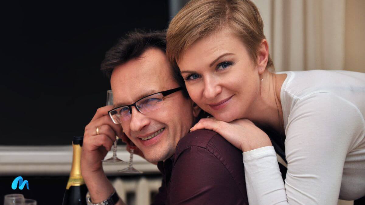 Couple in open air restaurant with man wearing specs and a maroon shirt with female resting her head on his shoulders-things mature women don't do in relationships