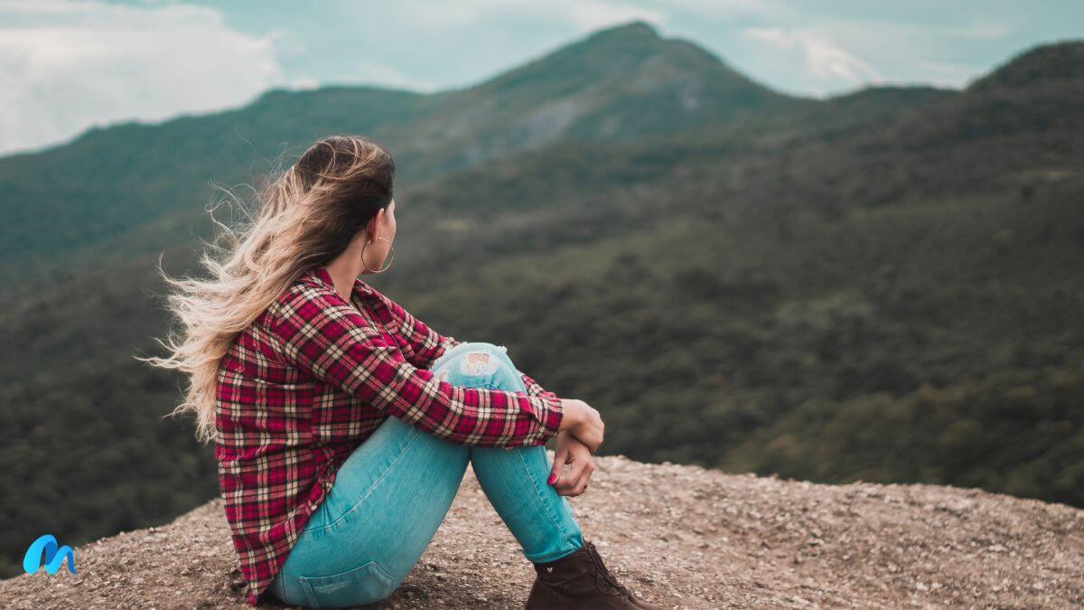 Young blonde women sitting on a hill in red check shirt and blue denim pants with wind blowing through her hair-i am broken