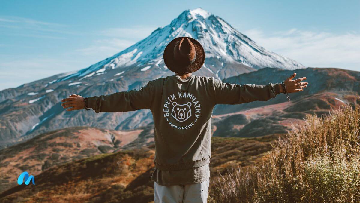 Man in grey t shirt looking towards a mountain and spreading his arms