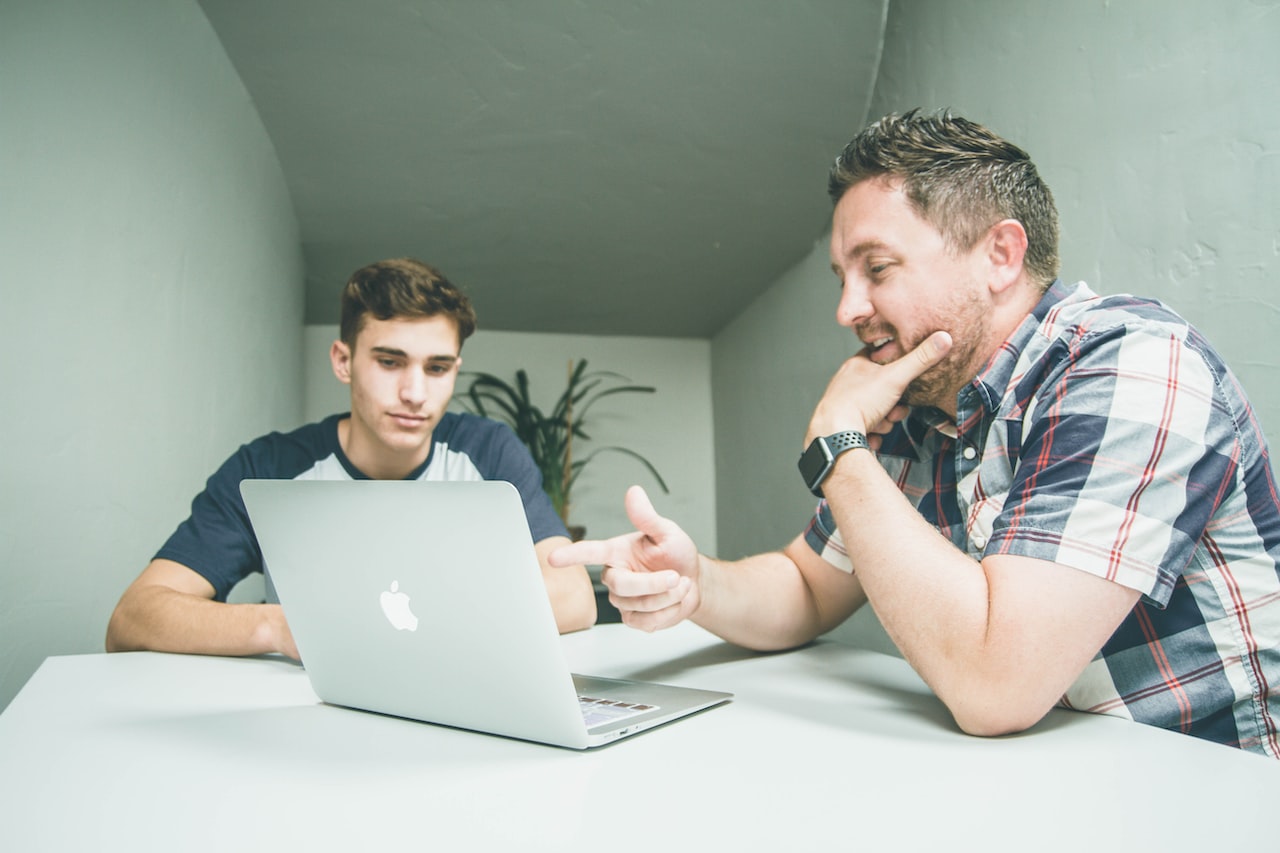 Man wearing white and black plaid button-up sports shirt pointing the silver macbook