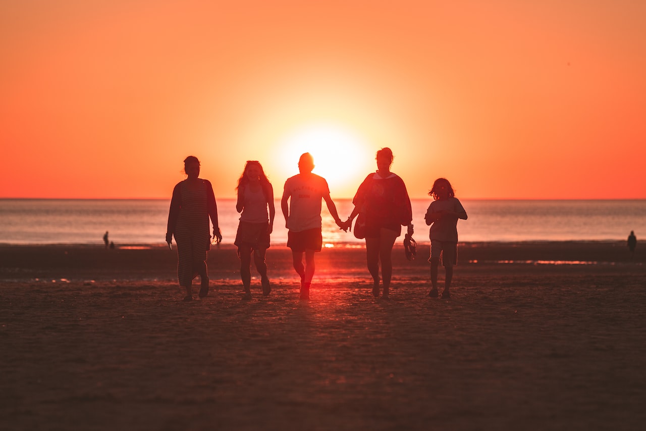 Silhouette photo of five person walking on seashore during golden hour