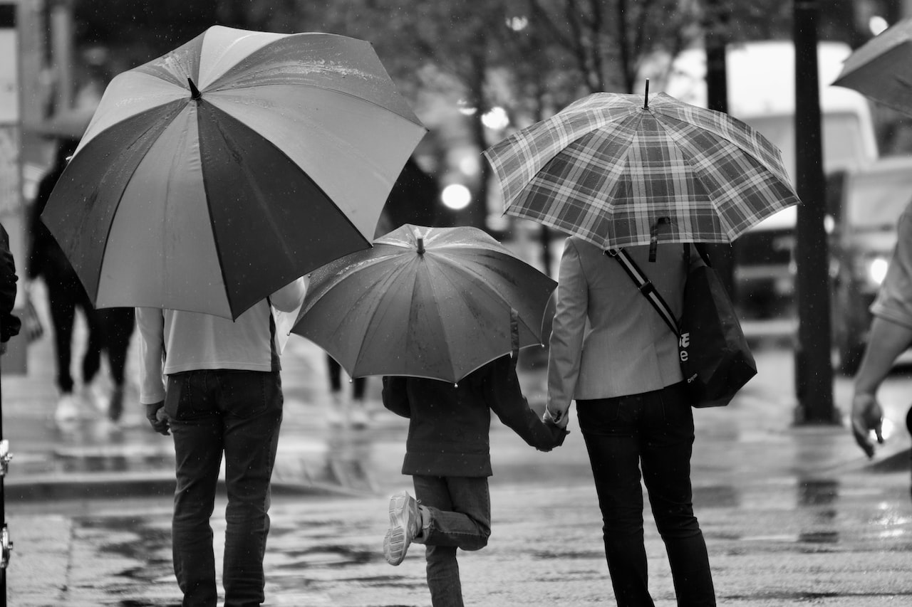 Grayscale photography of three person's holding umbrella