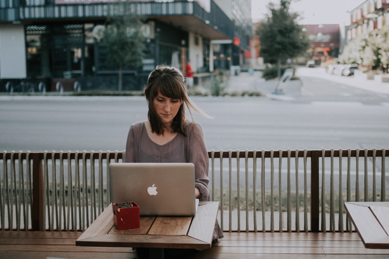 Woman in gray shirt sitting on bench in front of macbook