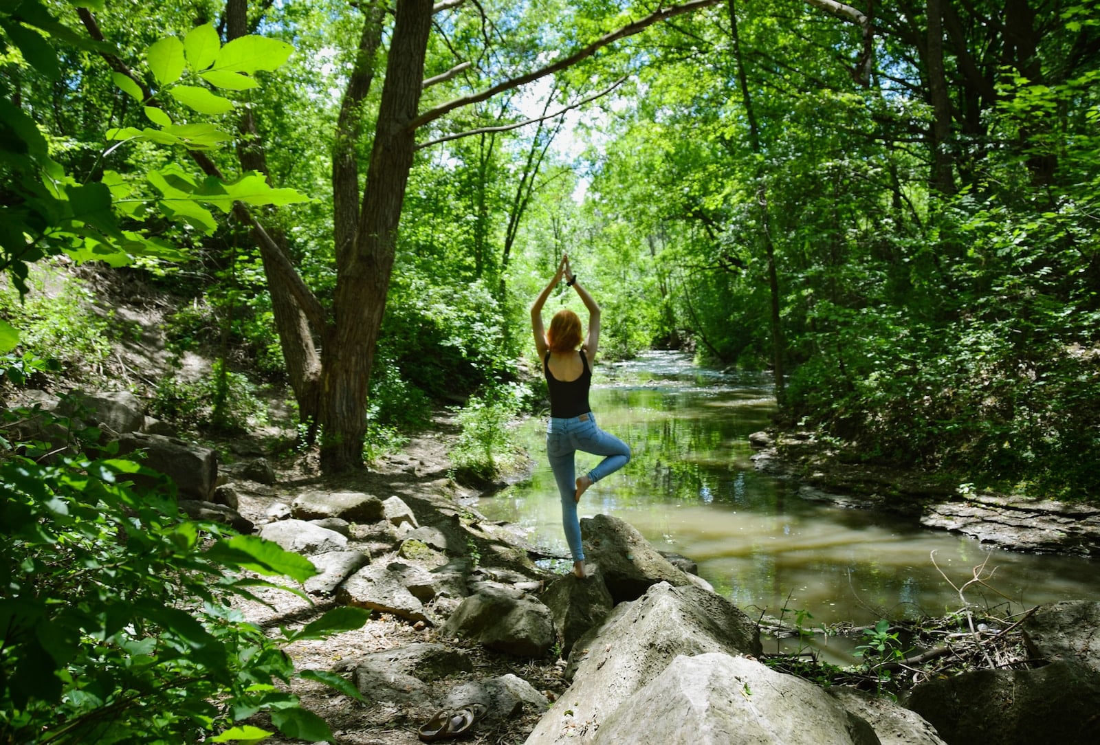 Woman in blue tank top and blue leggings standing on gray rock near river during daytime-healing power of nature