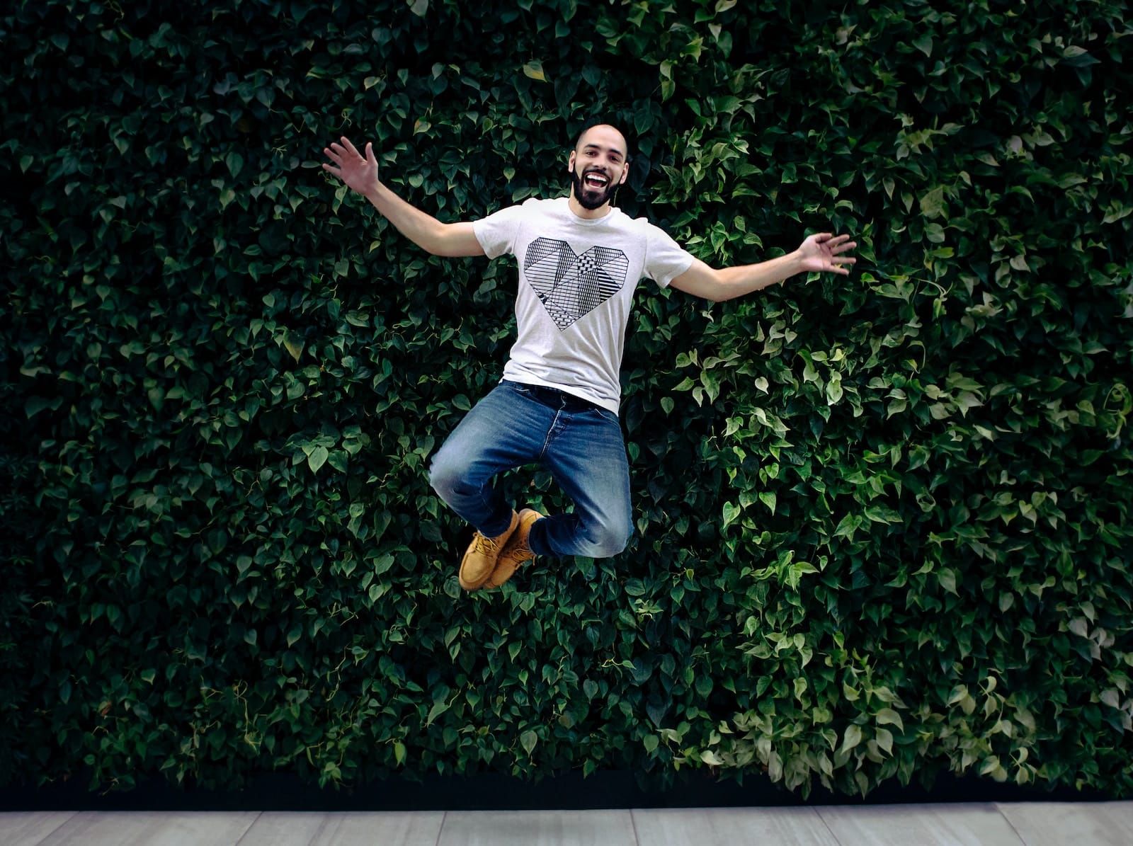 Man wearing t-shirt and jeans jumpshot in front of a green hedge-restore energy after work
