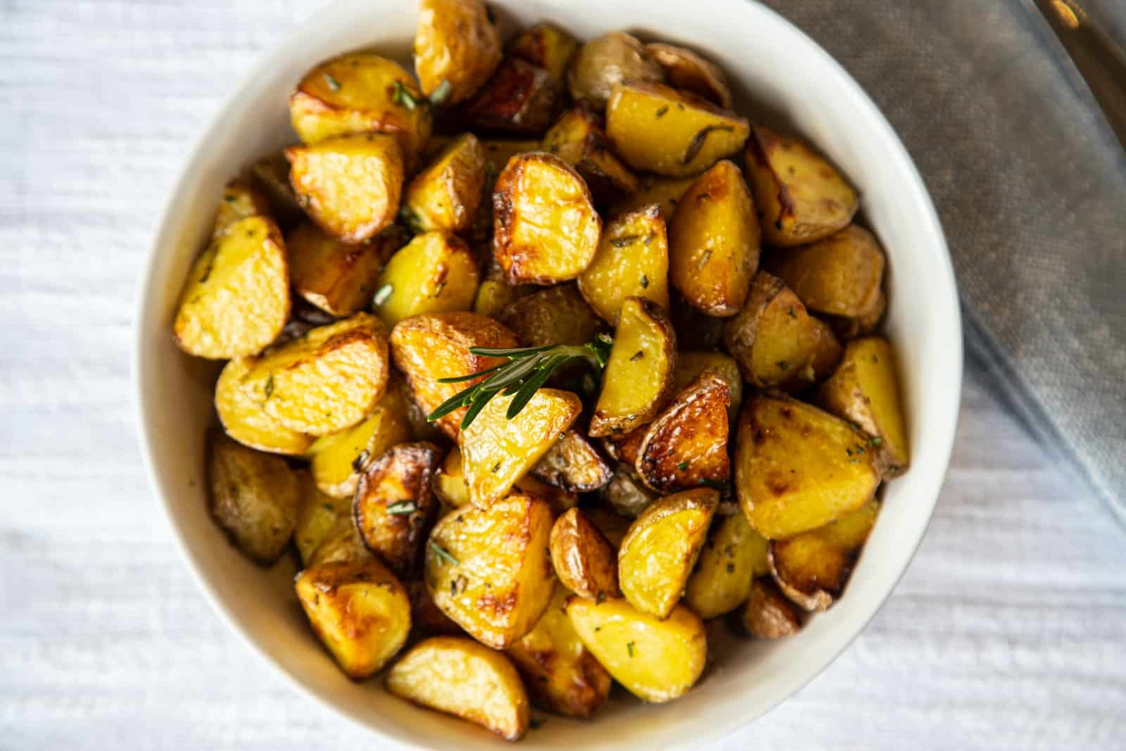 A white bowl filled with cooked potatoes on top of a table-are roasted potatoes healthy