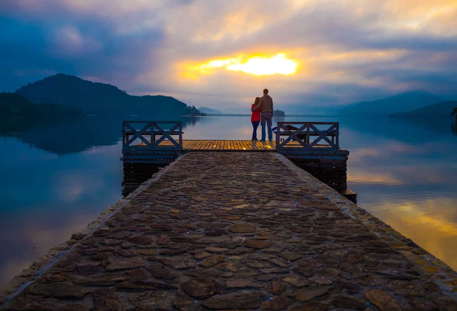 Couple standing on dock looking at sunset-secrets of everlasting love