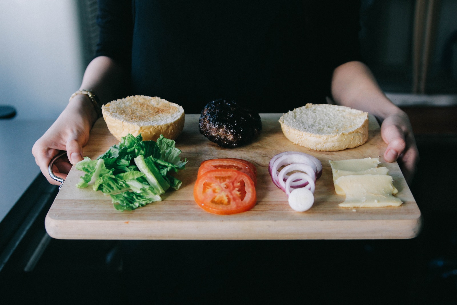 Woman holding up wooden tray with lettuce, tomato, onions rings and cooked patty for burger-why am i not hungry after not eating all day