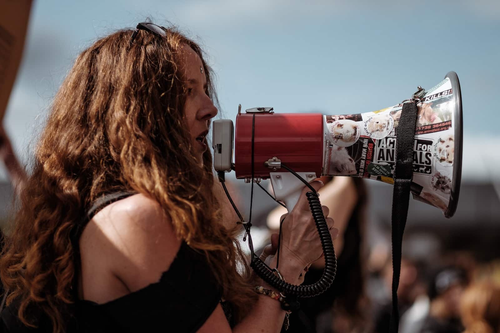 Selective focus photography of woman wearing black cold-shoulder shirt using megaphone during daytime-clarity in effective communication
