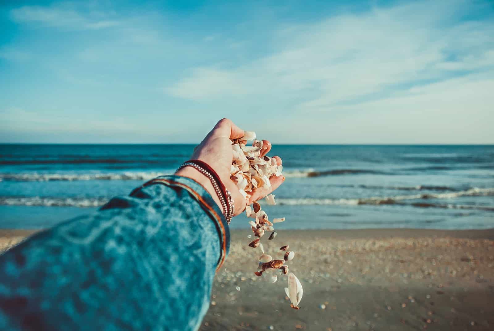 Person throwing seashells on seashore-let go of everything