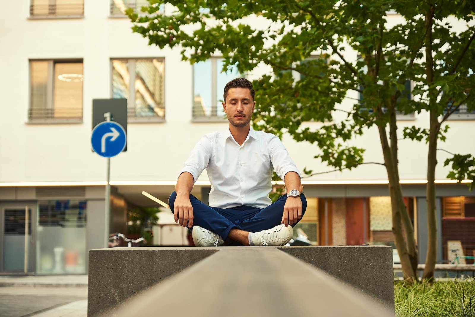 Man in white dress shirt sitting on gray concrete bench during daytime-how to solve your problems through meditation