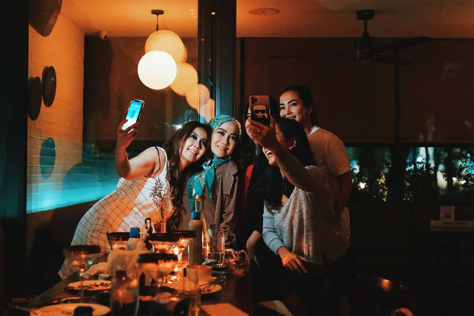 3 women smiling and standing near table-how to be more socially confident