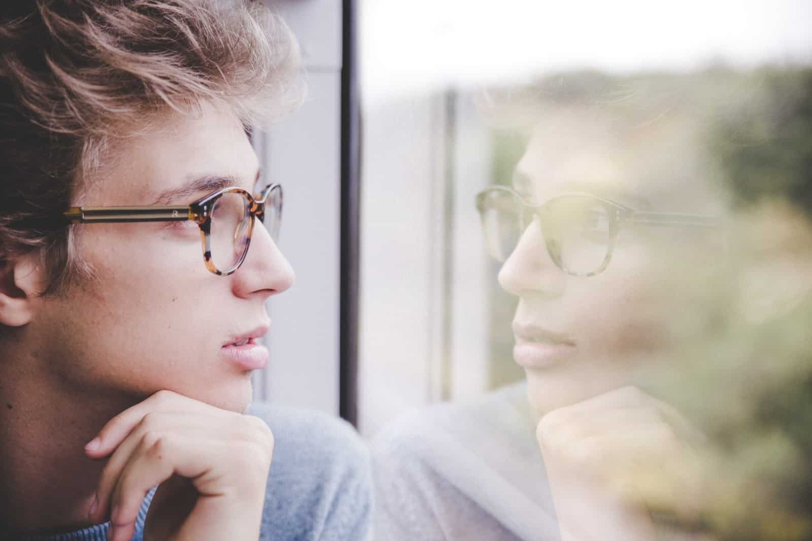 A man wearing glasses looking out a window-power of introspection