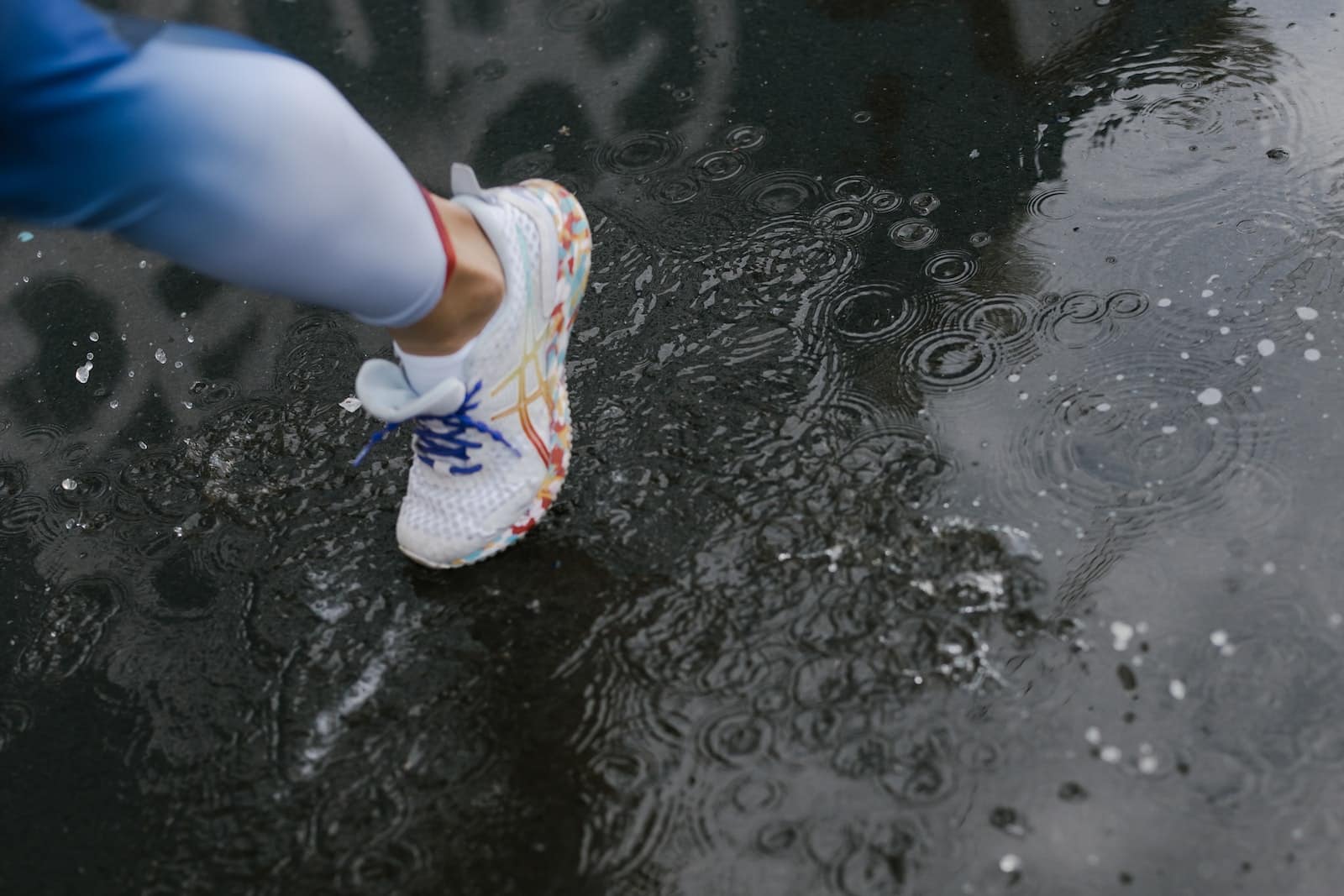 A person wearing a white shoes while stepping on wet road
