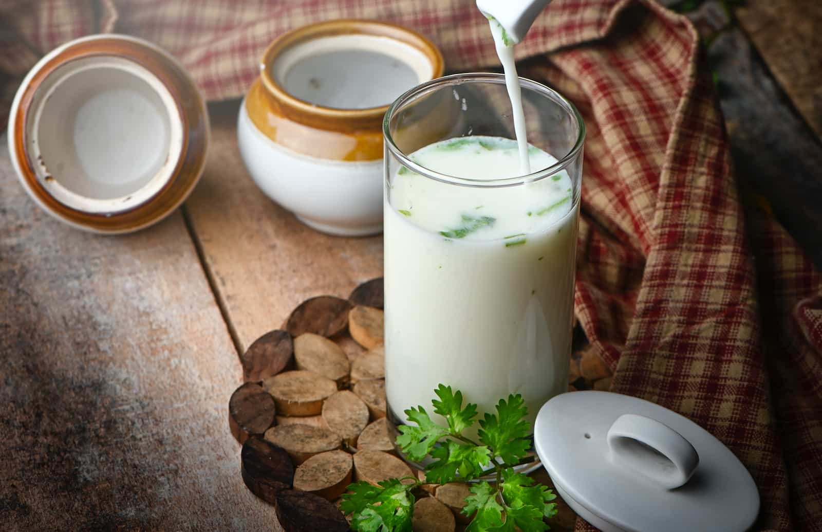Milk in clear drinking glass with green leaves and white cream-can you drink buttermilk