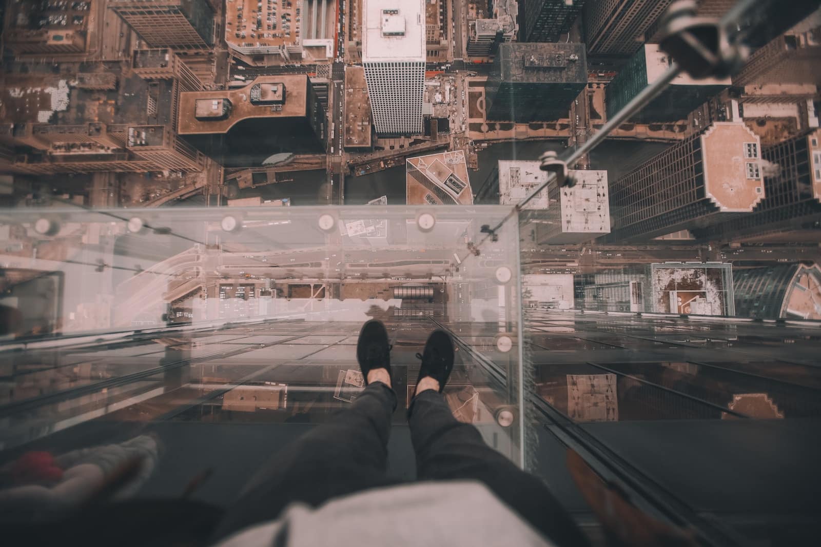 Man standing on glass platform on top of building looking down on ground at daytime-fear is the greatest motivator