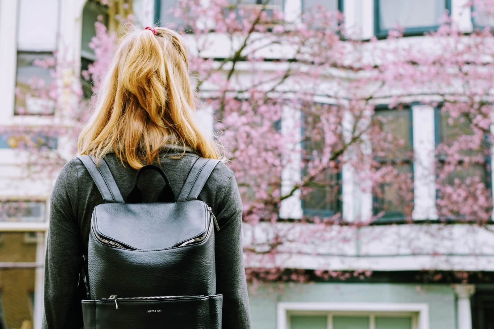 Woman wearing backpack facing concrete building-pursue educational and academic goals