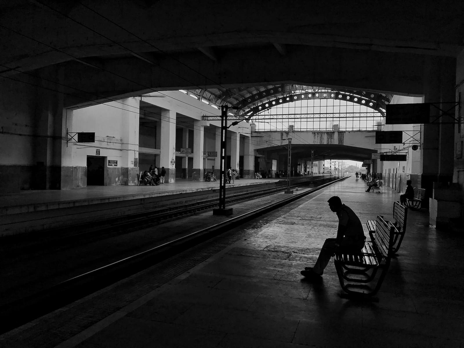 Silhouette of man sitting on bench beside train rail