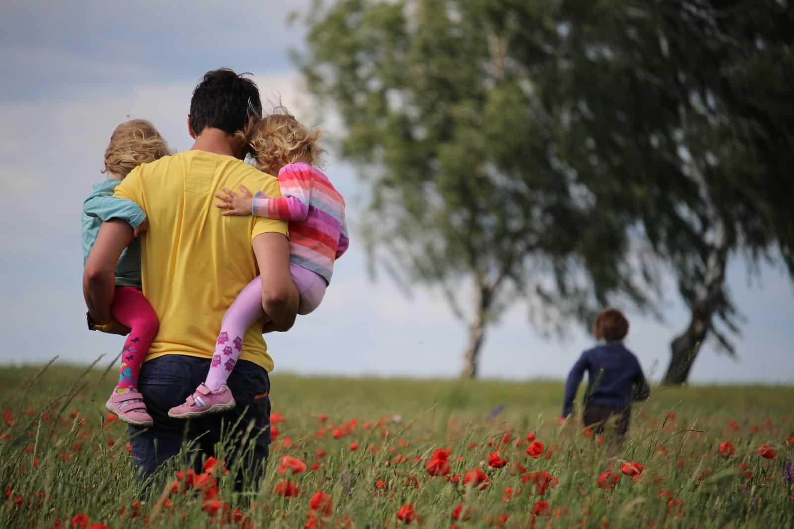 Man carrying to girls on field of red petaled flower-single father raising daughter