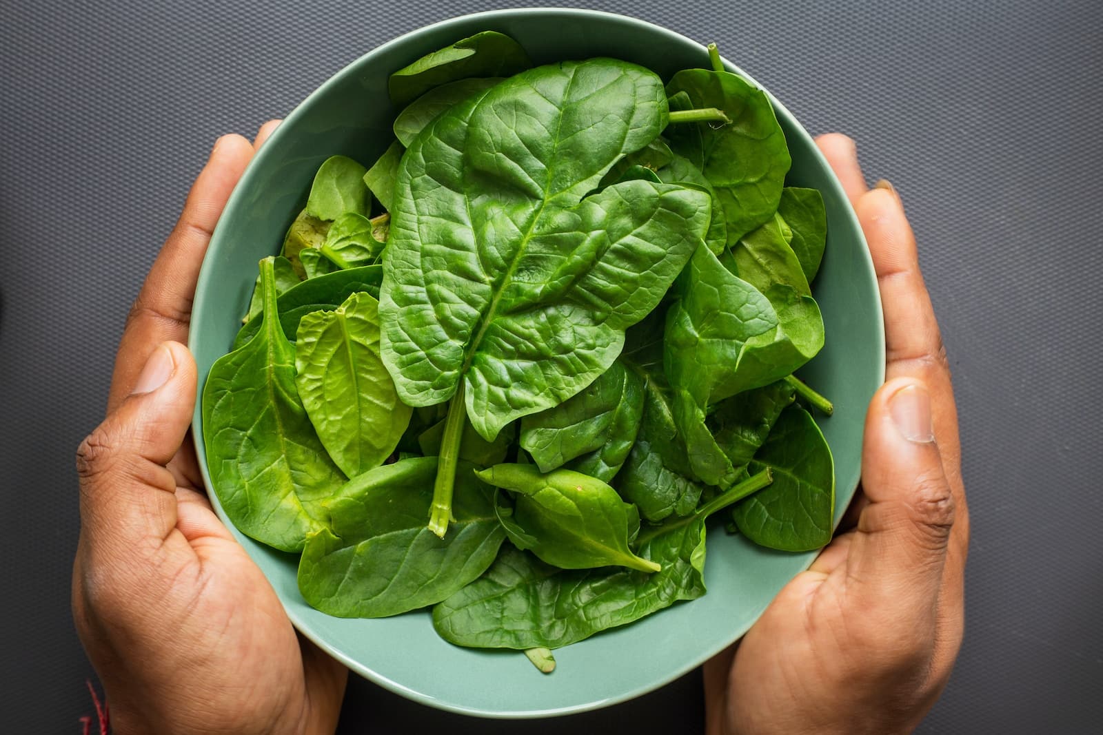 Green leaves on blue plastic bowl-unraveling the green mystery: is spinach to blame for your upset stomach? Discover the surprising truth behind this leafy culprit causing potential digestive distress.