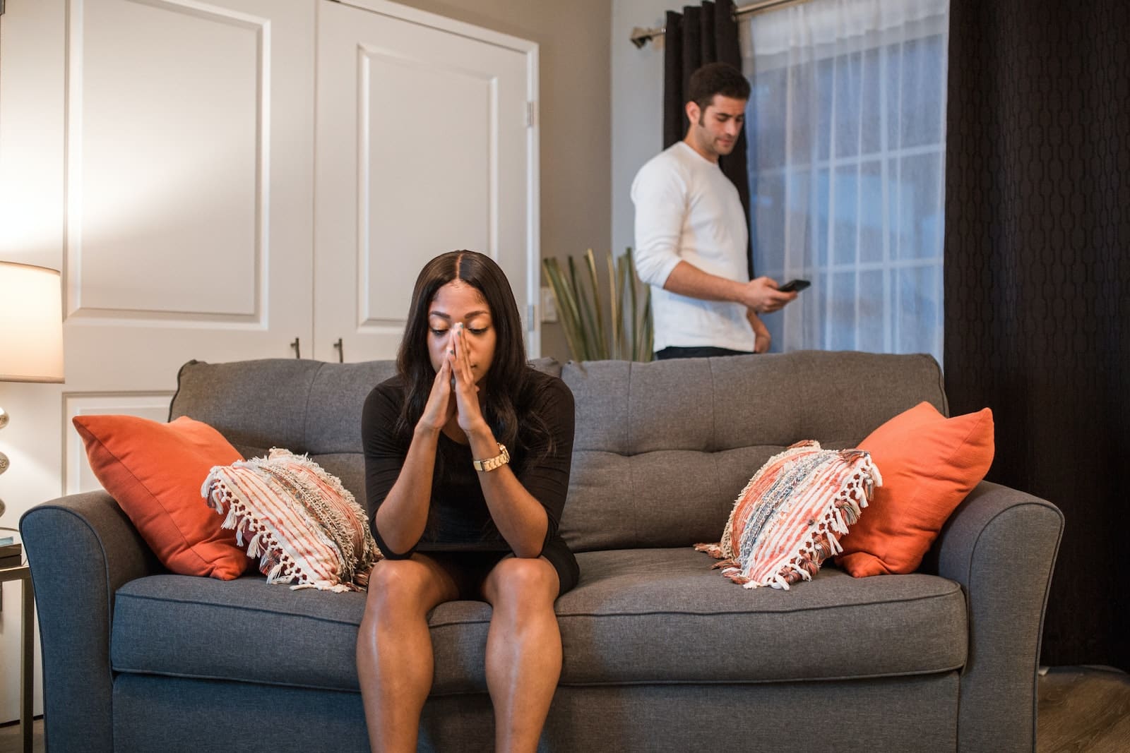 A woman sitting on the sofa while a man is standing at the back-breaking up from long-term relationship