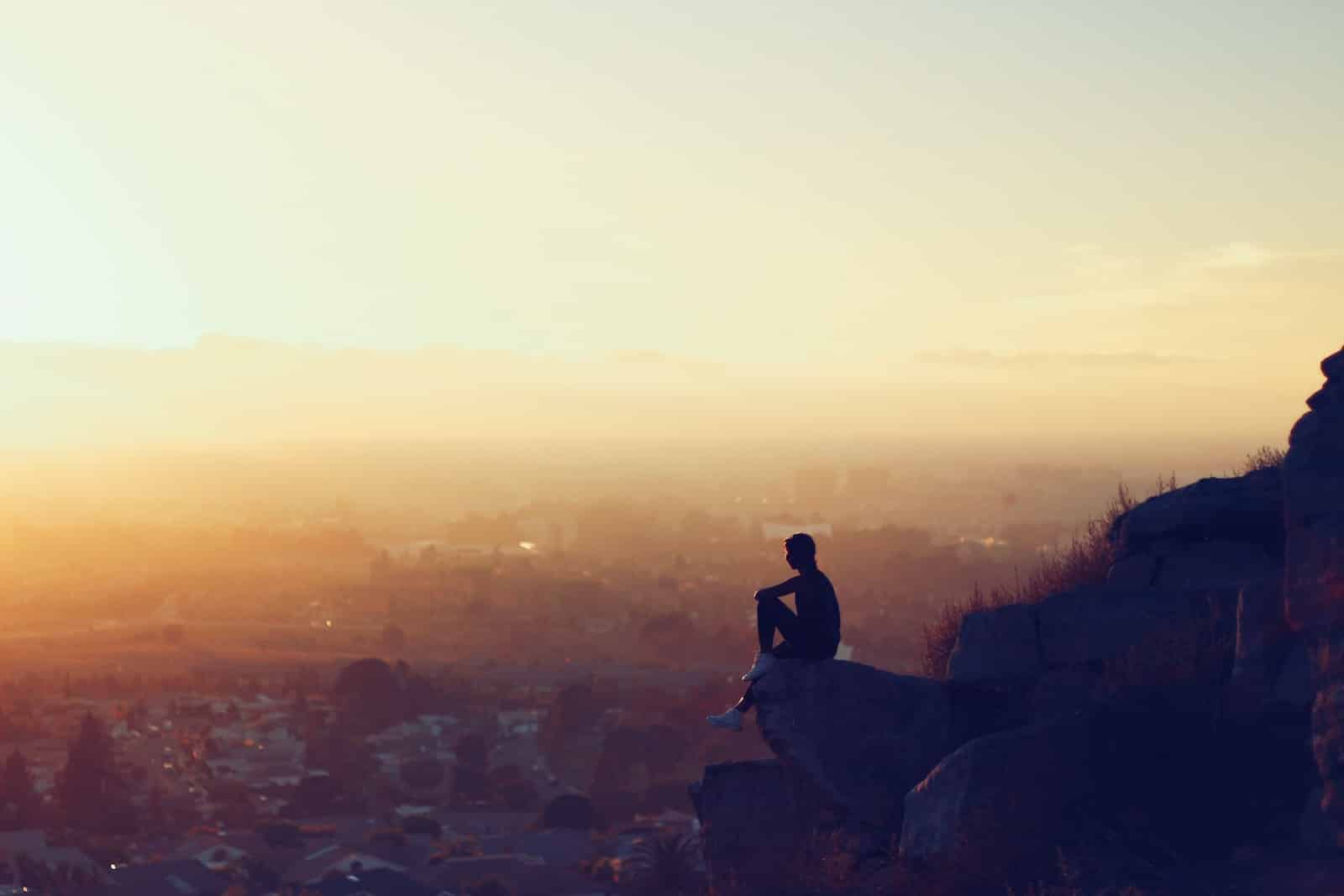 Man sitting on rock formation in cliff during golden hours-signs of inner conflict